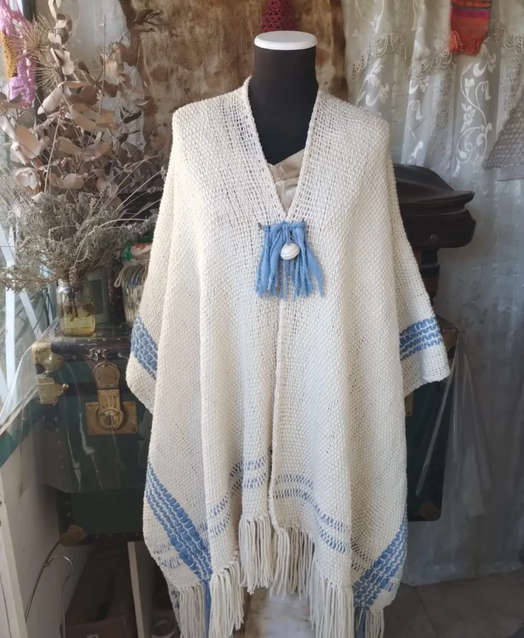 Poncho artesanal blanco con detalles azules exhibido en un maniquí para la Feria Revolución de Comodoro Rivadavia.