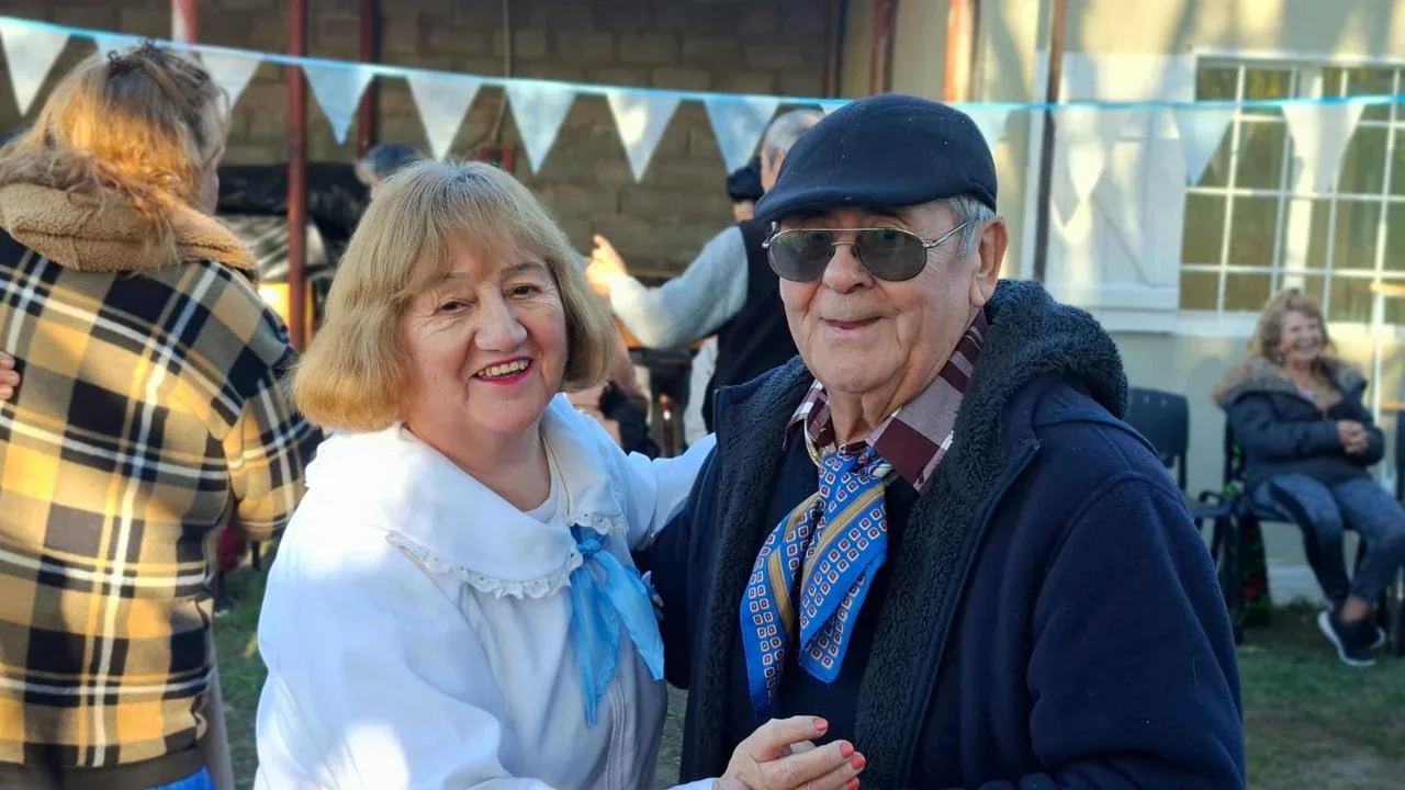 Pareja de personas mayores sonriendo en el encuentro del 25 de Mayo en el Centro de Día Papa Francisco, Comodoro Rivadavia.
