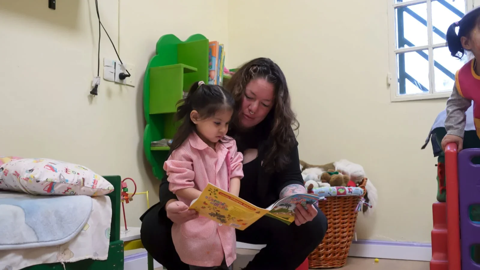 Una docente lee un libro colorido a una niña pequeña en el interior del CPB Diadema de Comodoro Rivadavia.