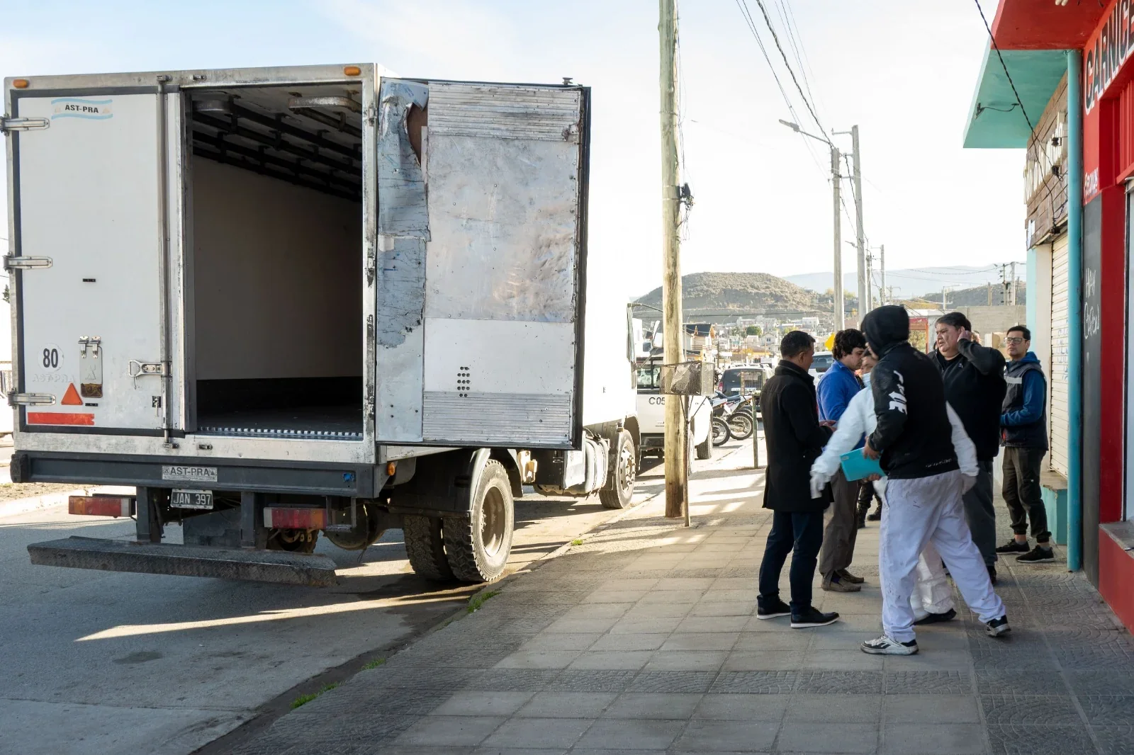 Camión de carga con puertas abiertas estacionado frente a un local, con inspectores municipales y el conductor.