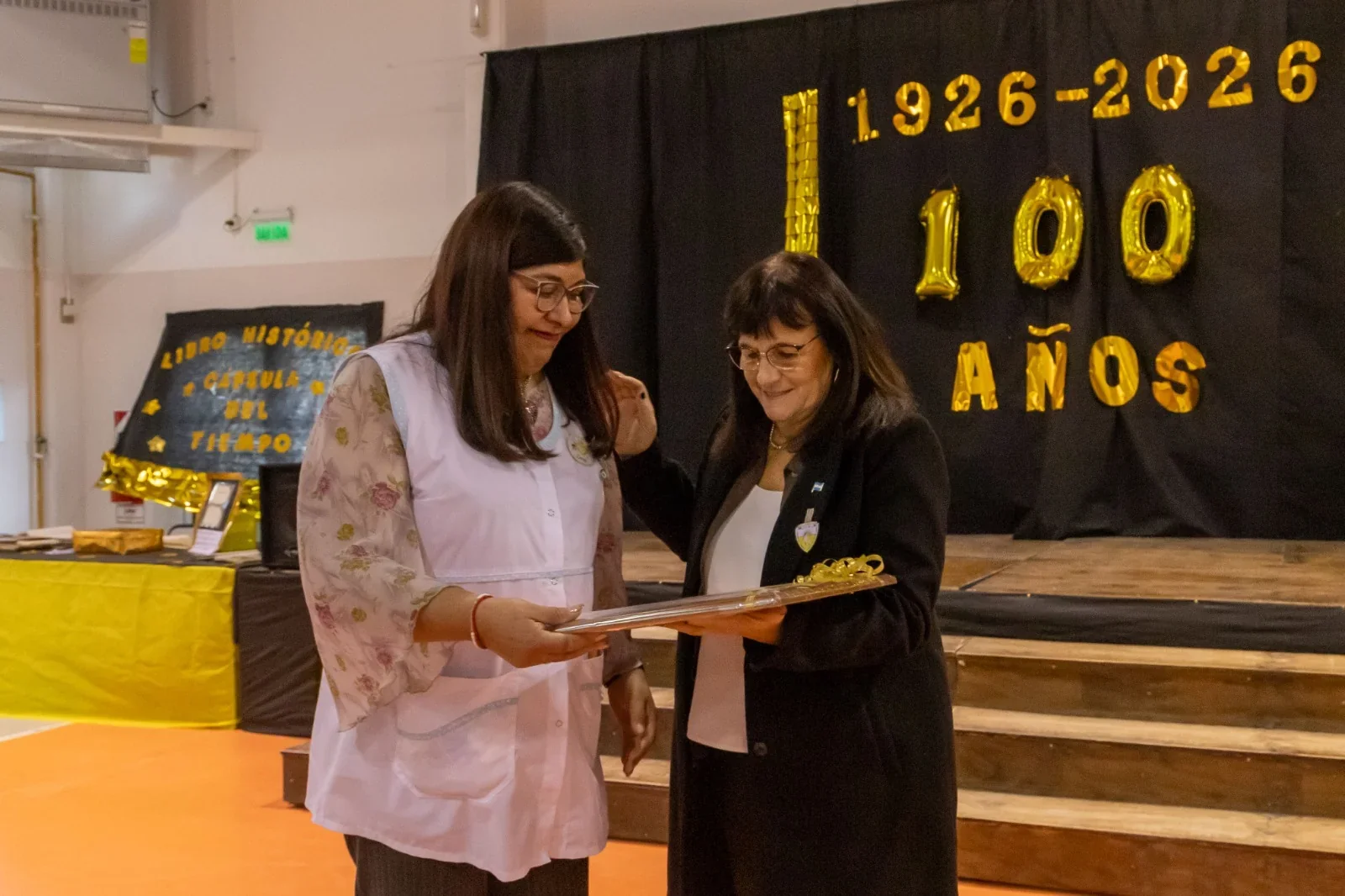 Dos mujeres sostienen una placa conmemorativa durante el acto del centenario de la Escuela N° 91 en Comodoro Rivadavia.