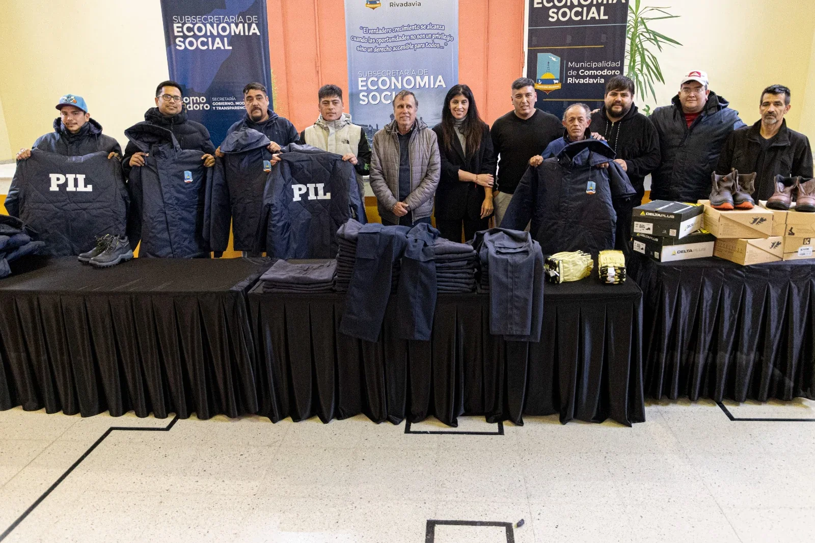 Grupo de personas junto a indumentaria laboral con siglas PIL y calzado sobre una mesa en Comodoro Rivadavia.