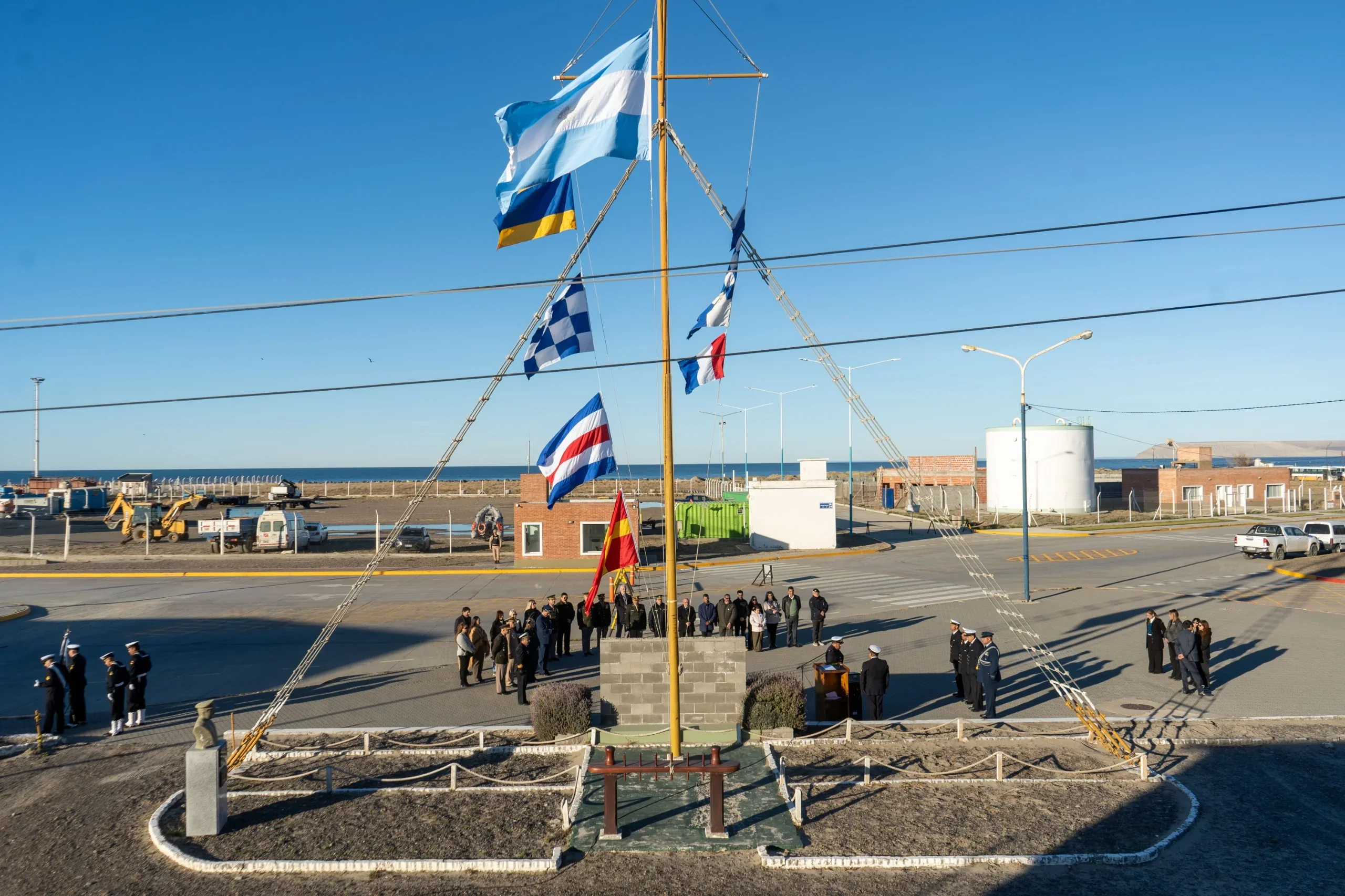 Acto oficial por el 212° aniversario de la Armada Argentina en la Plaza de Armas de Comodoro Rivadavia con banderas izadas.