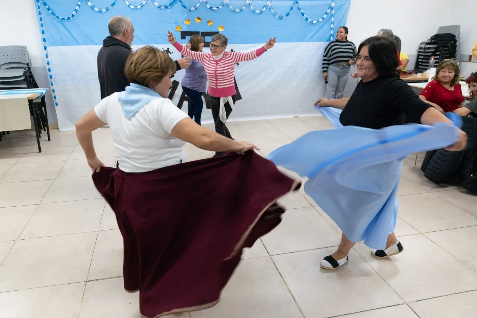 Adultos mayores de los grupos A.M.O. y Huellas de Abril bailan con telas celestes y blancas en Comodoro Rivadavia.