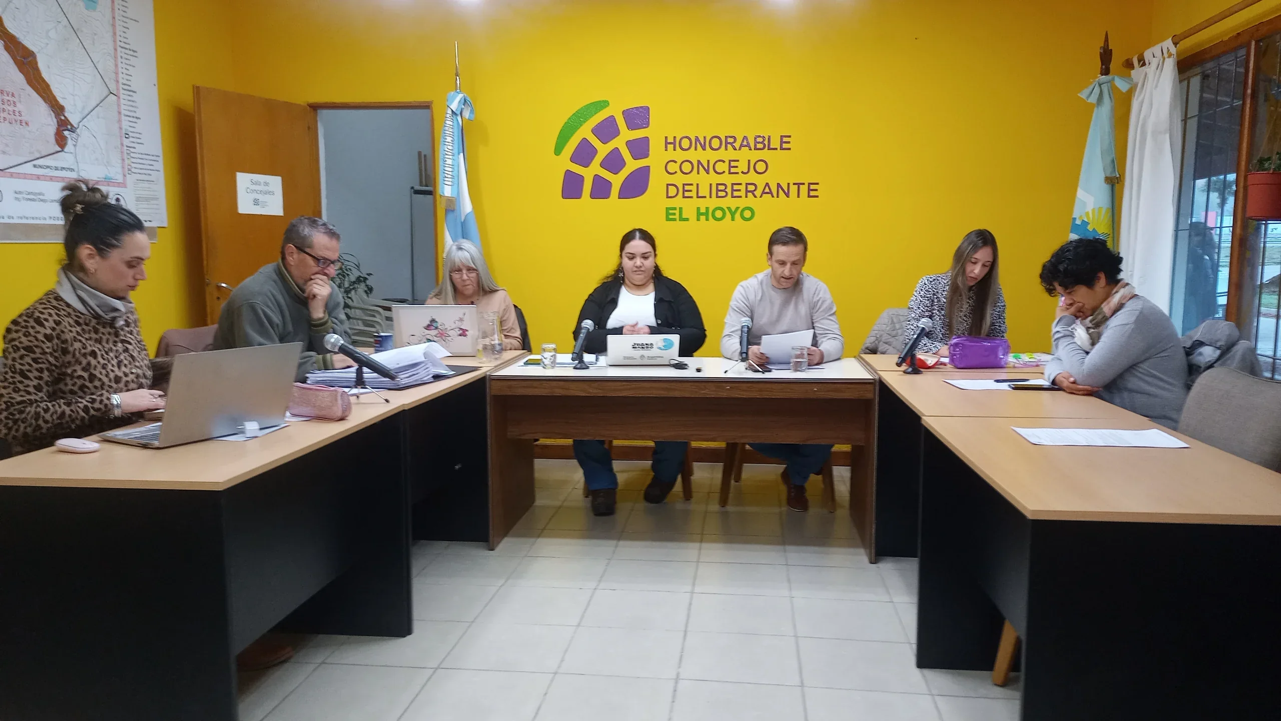 Sesión del Concejo Deliberante de El Hoyo con concejales reunidos en una mesa de trabajo frente a una pared amarilla.