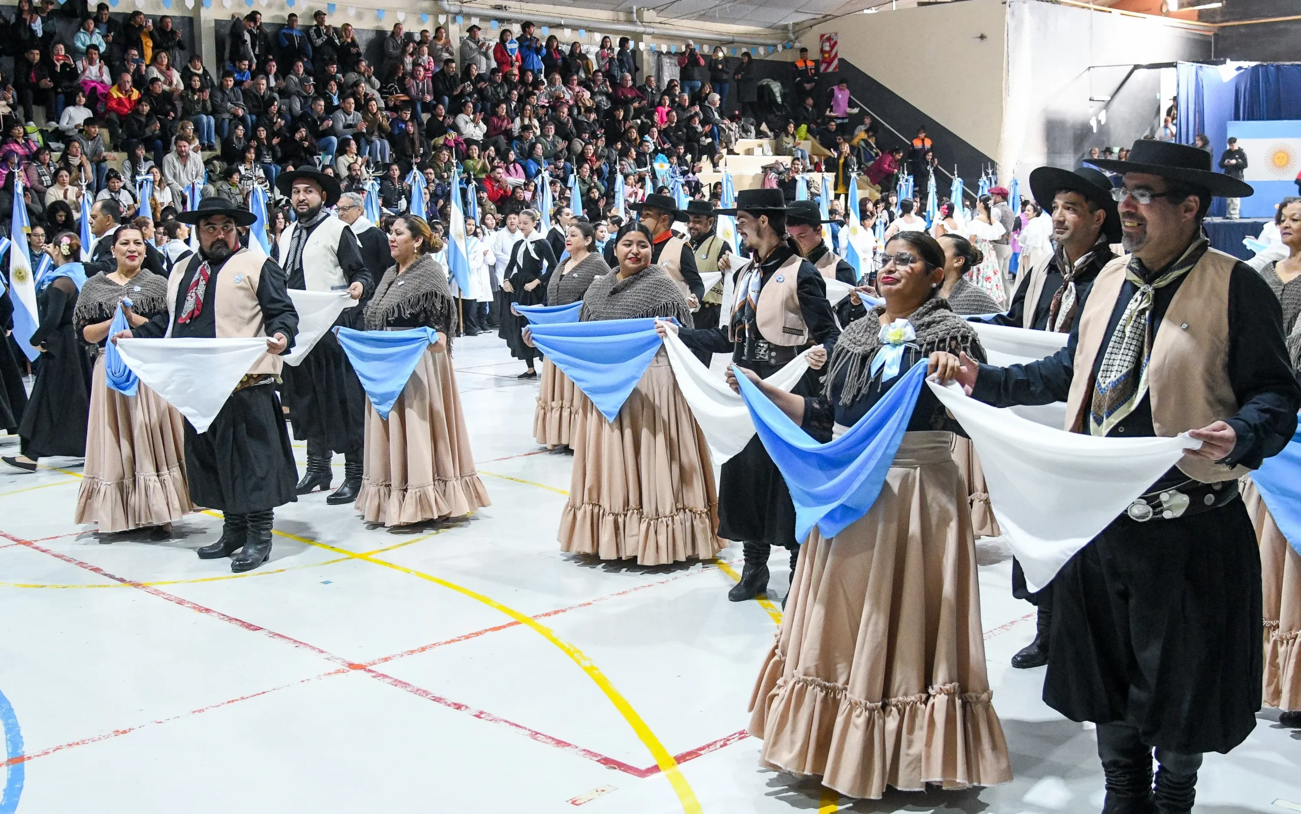Bailarines de la Escuela El Pampero con trajes típicos y banderas argentinas en el Gimnasio Municipal de Puerto Madryn.