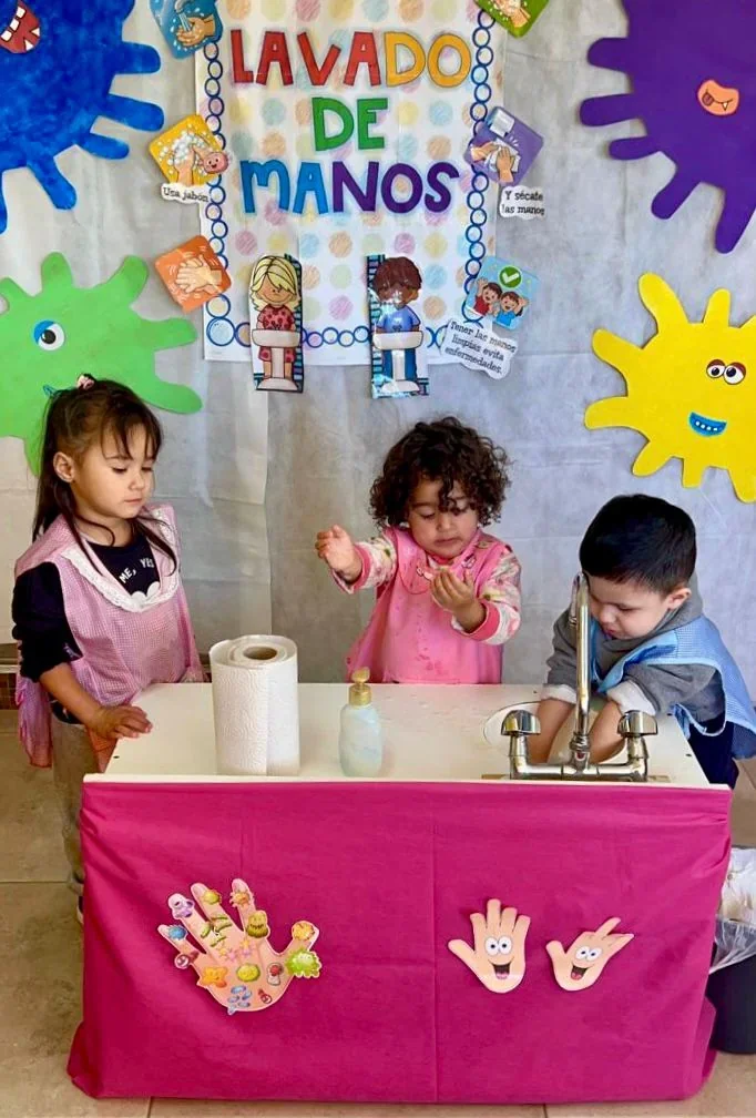 Tres niños aprenden el lavado de manos frente a un panel educativo en un Centro de Primera Infancia de Puerto Madryn.