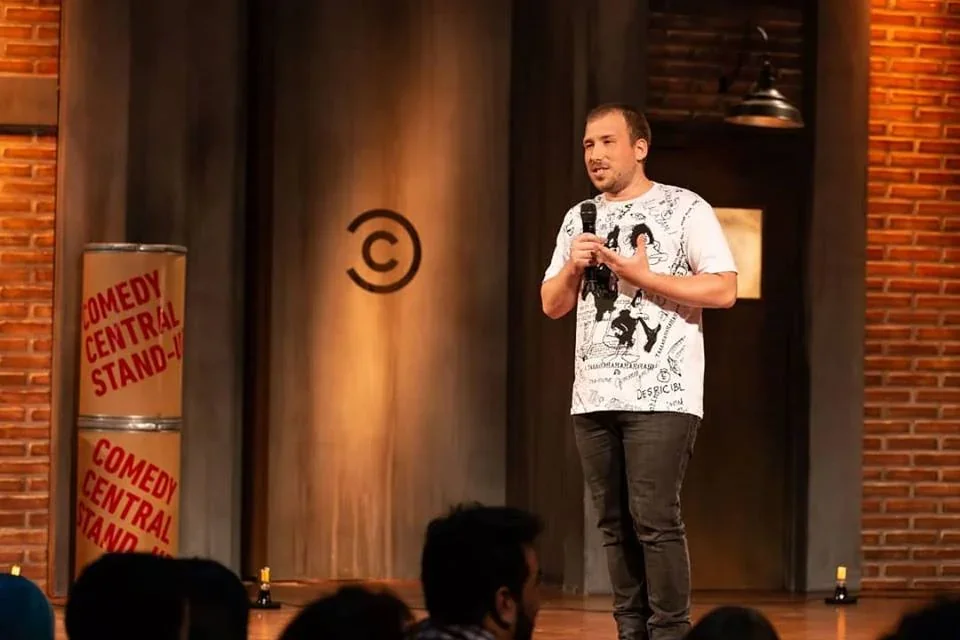 Lucas Upstein realizando un show de stand up con micrófono en mano sobre un escenario de Comedy Central.