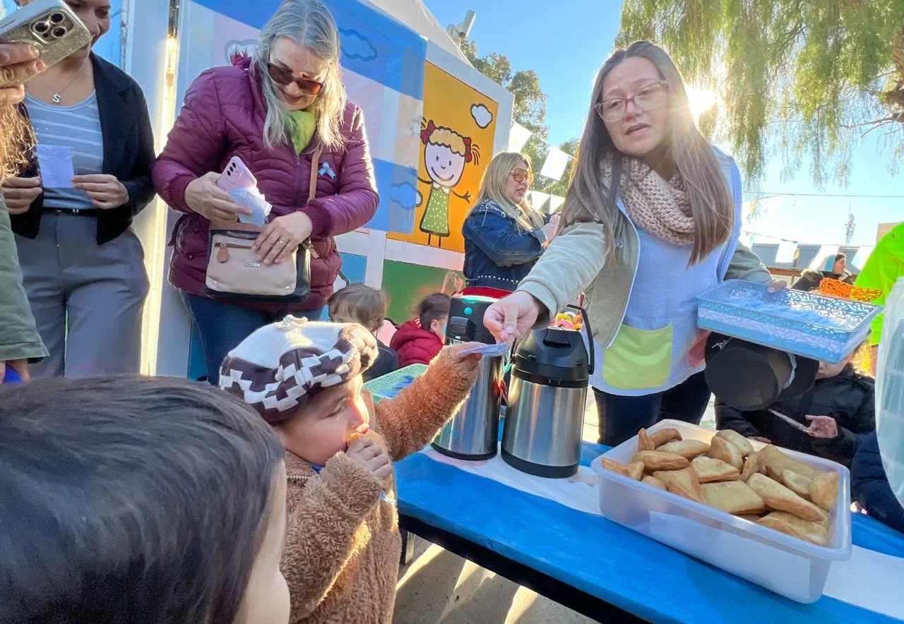 Niños y adultos del CPI Evita comparten un desayuno patrio en una mesa con termos y comida en Puerto Madryn.