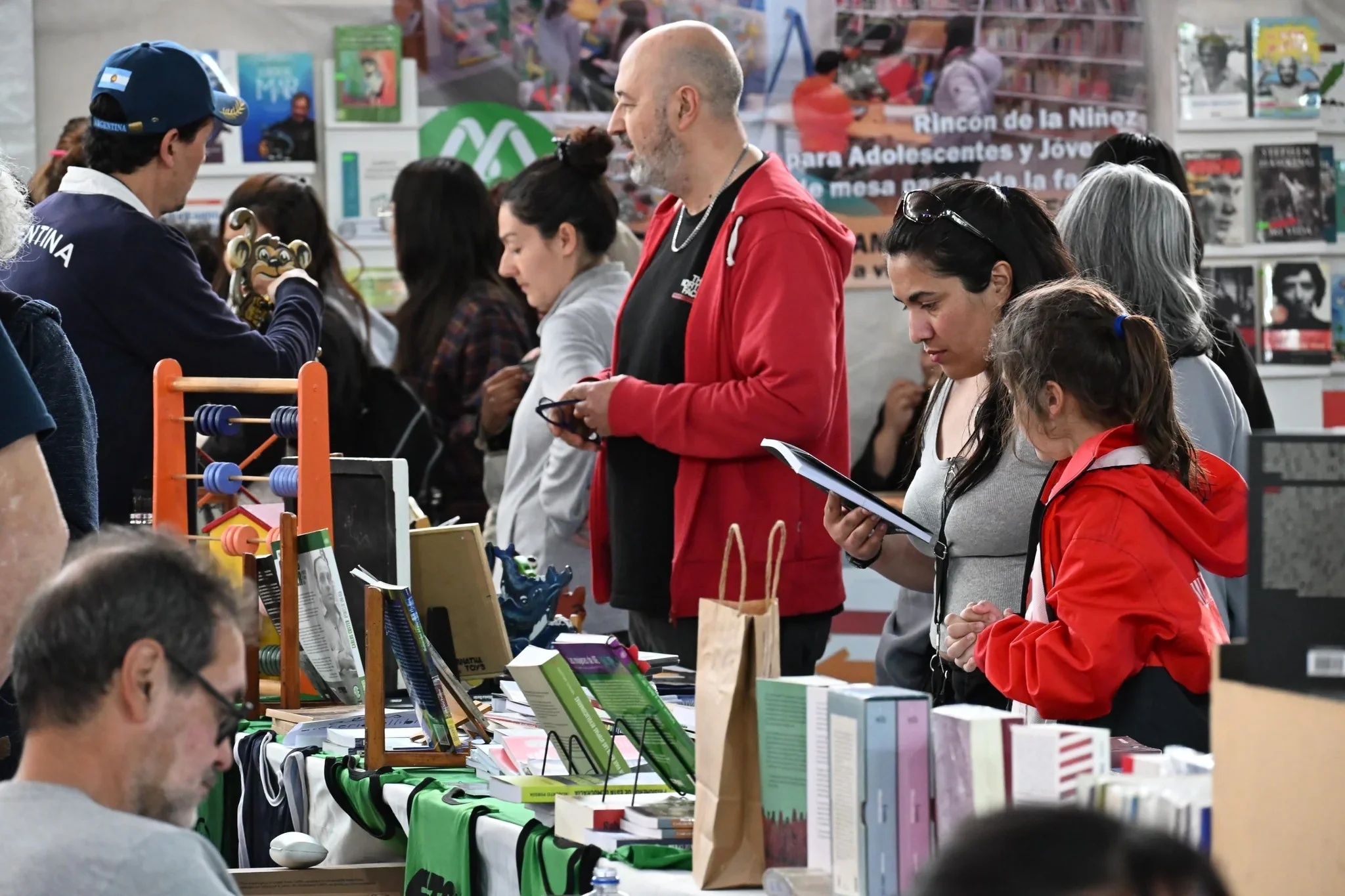Personas de diversas edades recorren un stand con libros y materiales educativos en la Feria del Libro de Puerto Madryn.