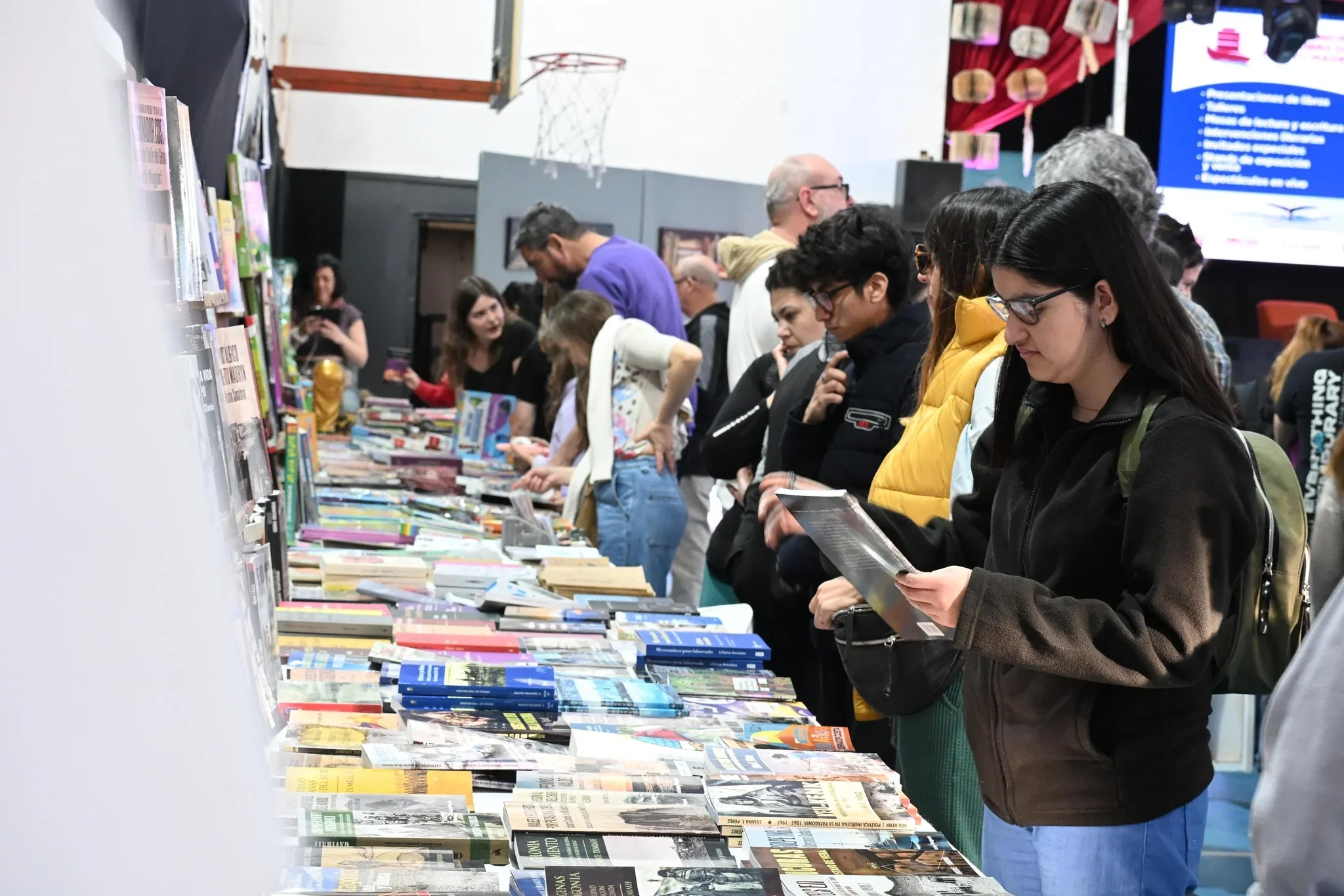 Personas recorriendo un stand con libros expuestos en mesas durante la Feria Municipal del Libro de Puerto Madryn.