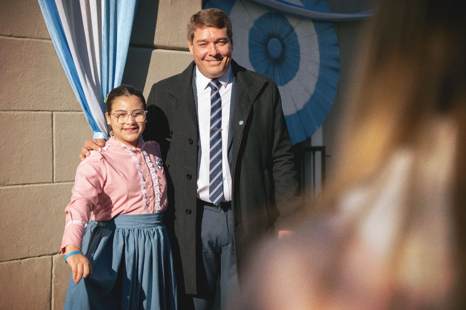 El intendente Damián Biss junto a una niña vestida con traje colonial en el acto por la Revolución de Mayo en Rawson.