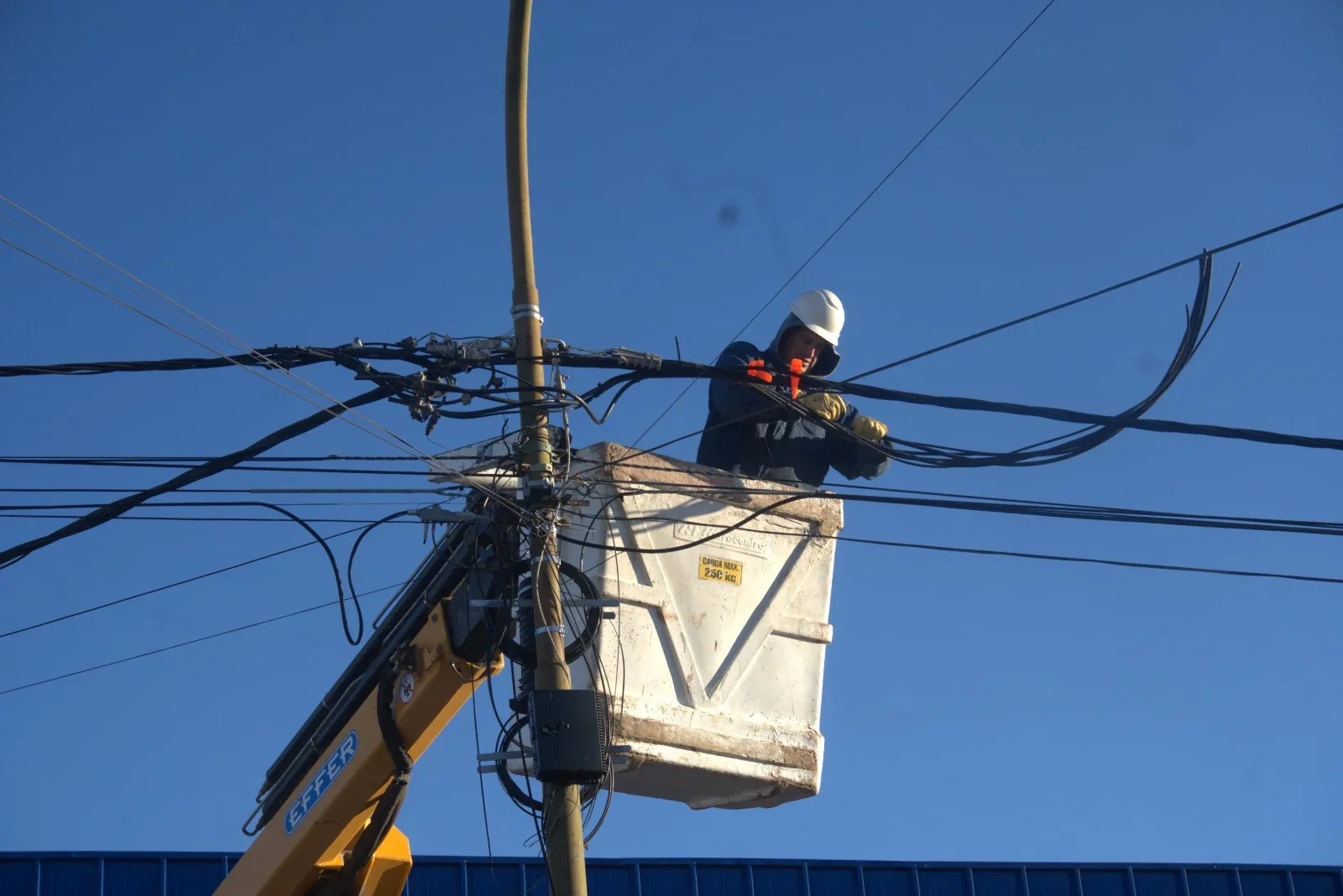Técnico de la Cooperativa de Rawson trabajando en el cableado eléctrico desde una canastilla elevadora en Chacra 8.