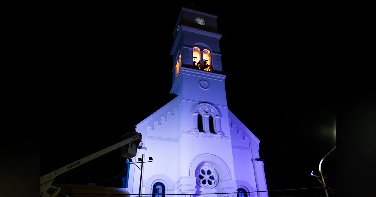Rawson: Cooperativa iluminó la Parroquia María Auxiliadora Fachada de la Parroquia María Auxiliadora de Rawson iluminada con luces azules y amarillas durante la noche.