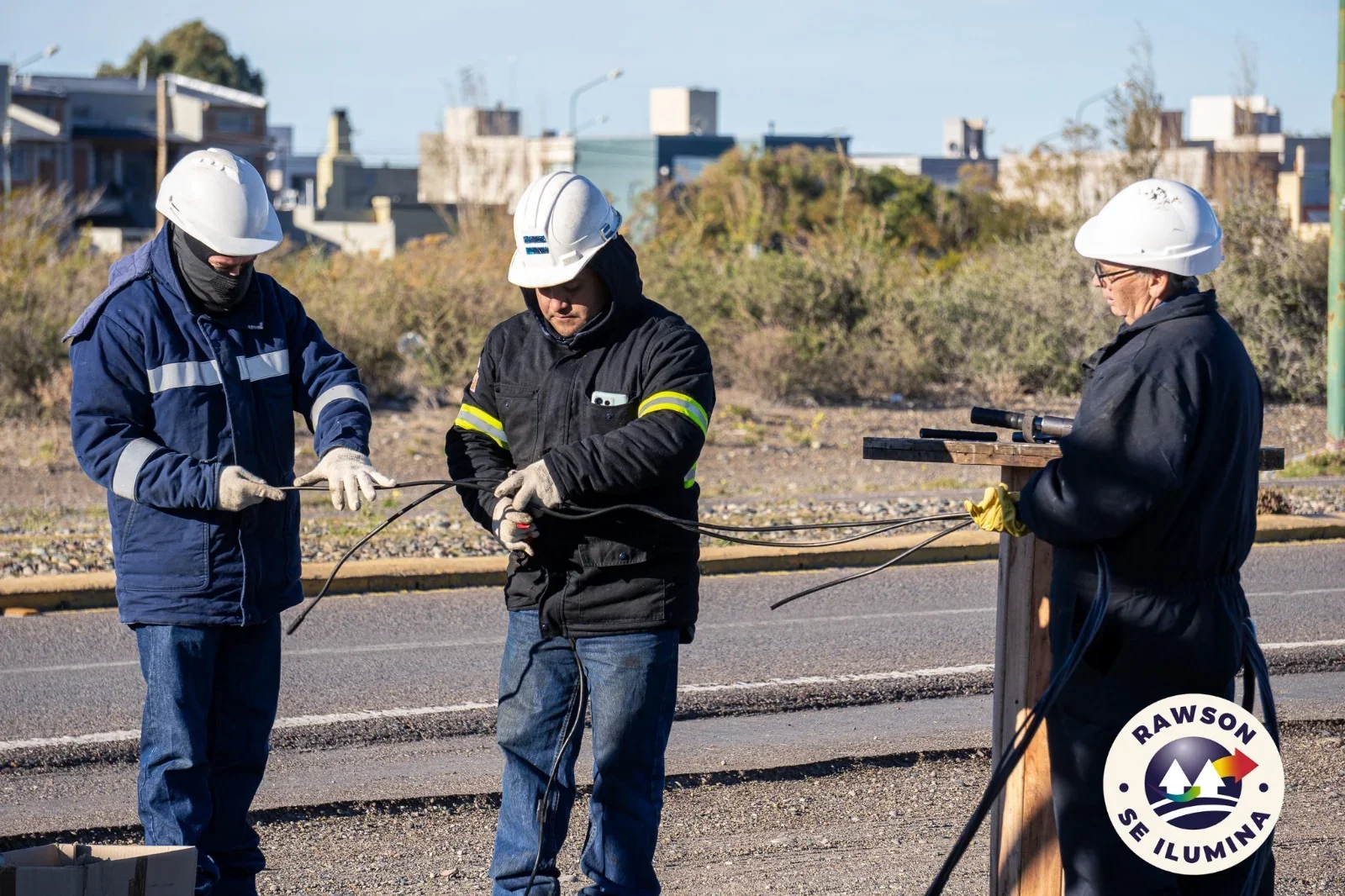 Tres operarios de la Cooperativa con cascos y ropa de trabajo realizan el tendido eléctrico en avenida Marcelino González.