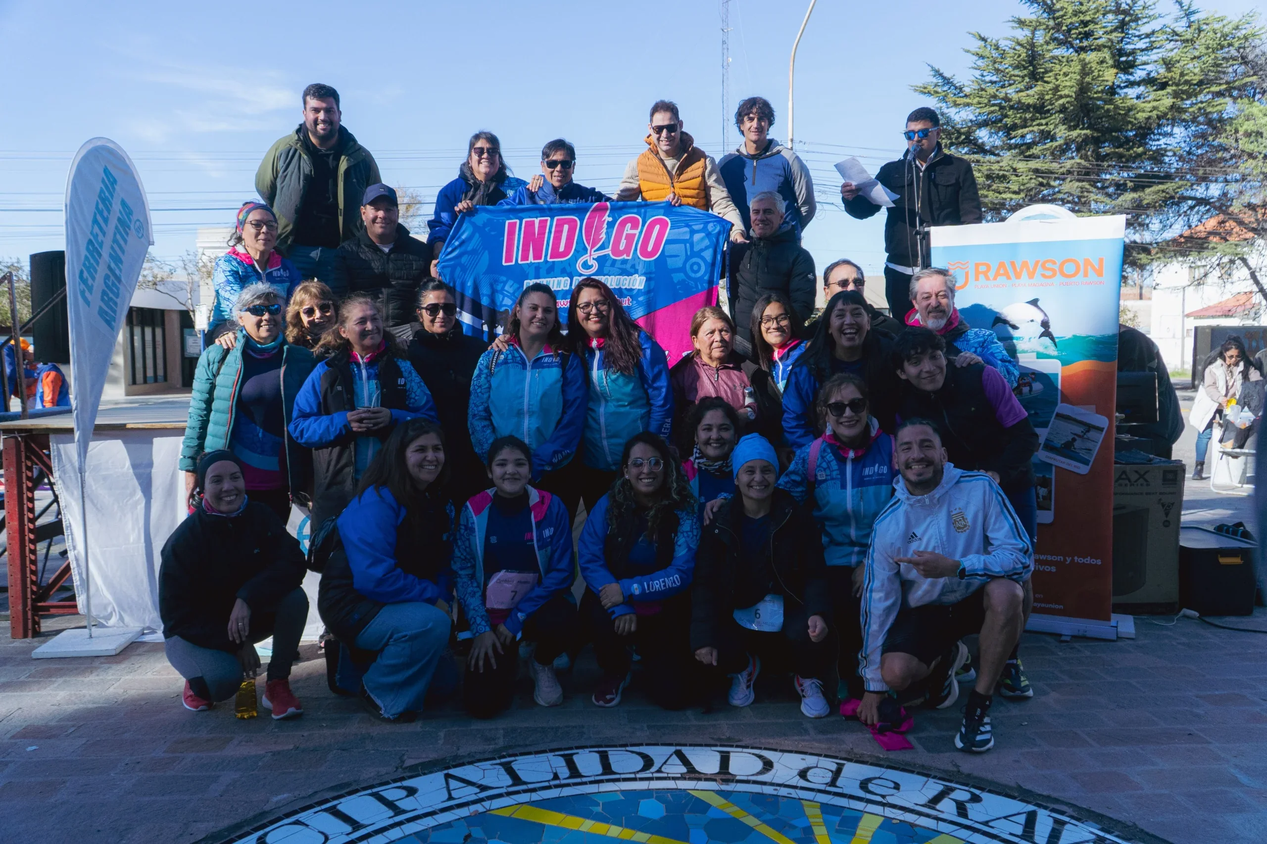 Grupo de personas con ropa deportiva y una bandera de Indigo en la primera Corrida de los Clubes en Rawson.