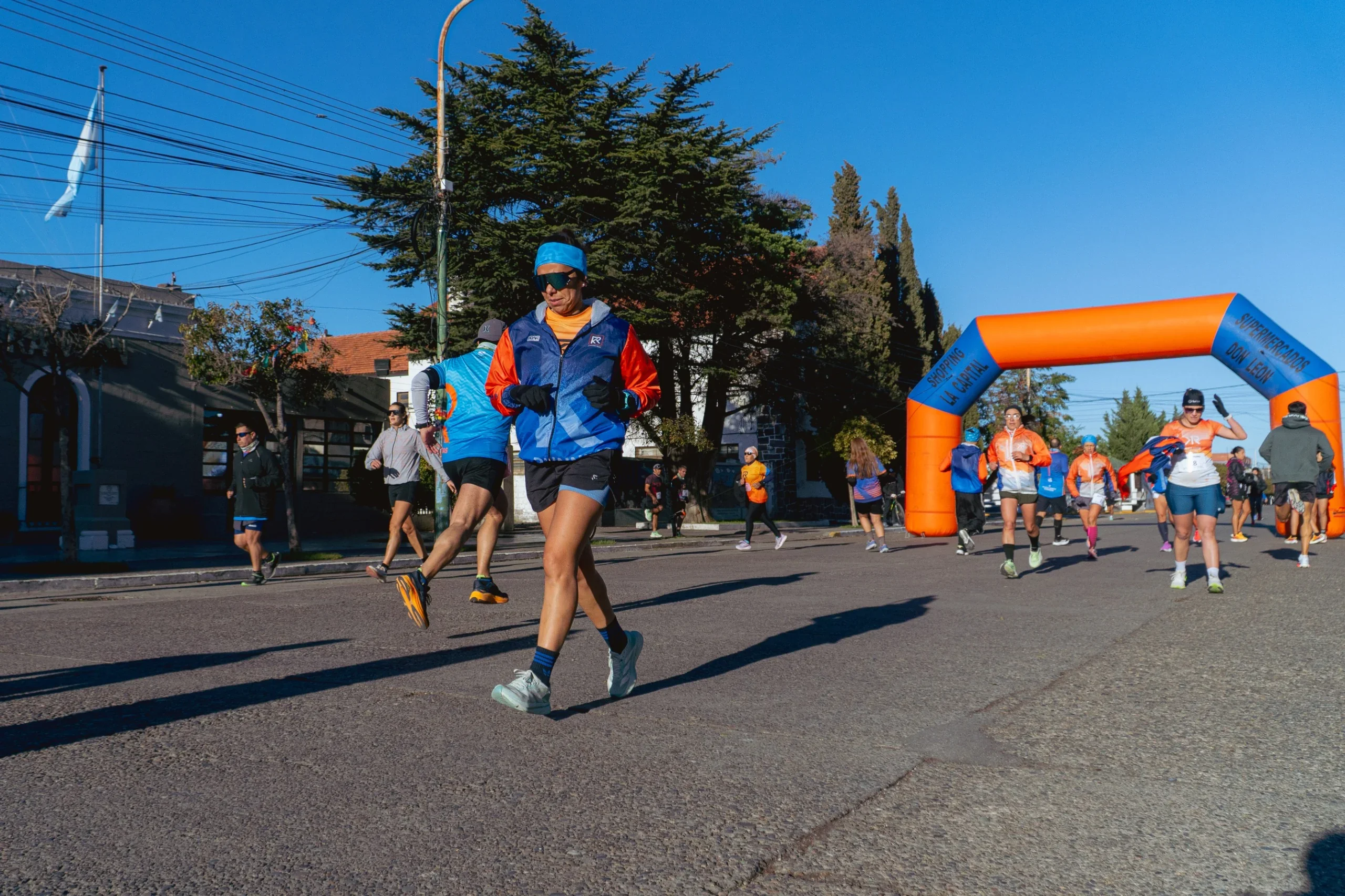 Atletas participando en la primera edición de la Corrida de los Clubes en Rawson, pasando por un arco inflable naranja.