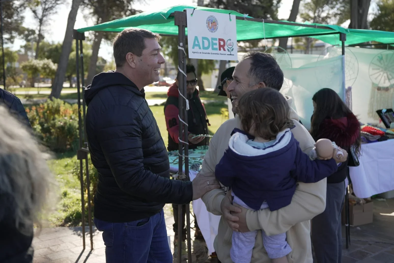 El intendente Damián Biss conversa con un productor que sostiene a un niño en la 4° Expo Capital en Rawson.
