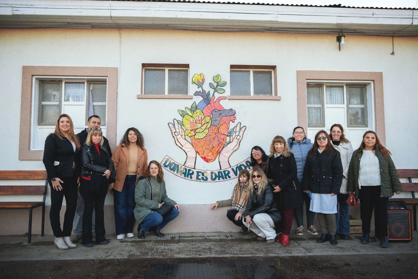 Grupo de personas posando frente al mural comunitario "Donar es Dar Vida" en el Hospital Santa Teresita de 