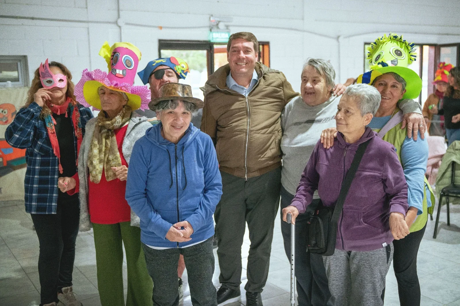 El intendente Damián Biss posa sonriente junto a adultos mayores con sombreros coloridos en la Colonia Recreativa de Rawson.