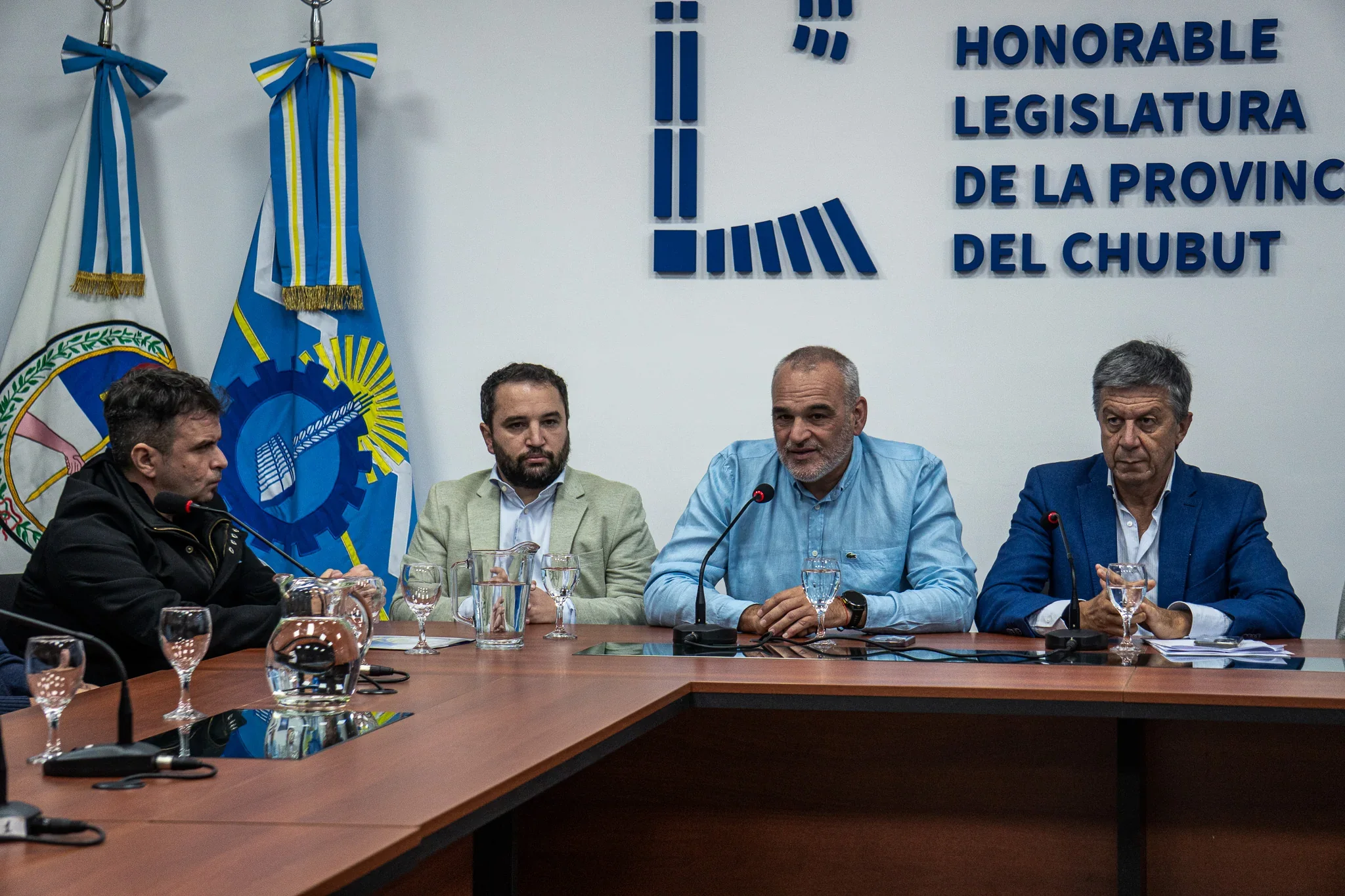 Autoridades y funcionarios en una mesa de prensa frente al logo de la Honorable Legislatura de la Provincia del Chubut.