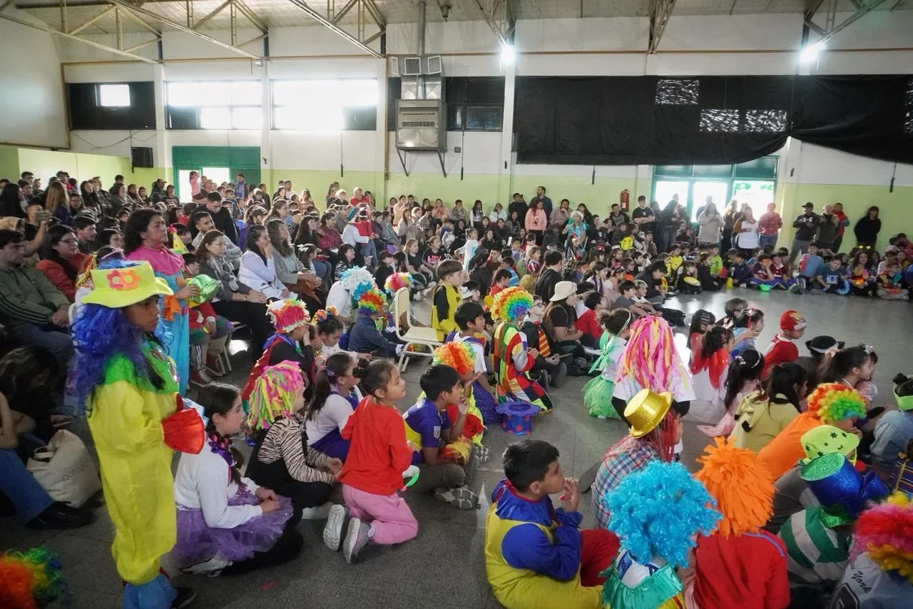 Estudiantes con pelucas coloridas y disfraces sentados en el SUM de la Escuela N° 202 de Rawson durante su aniversario.