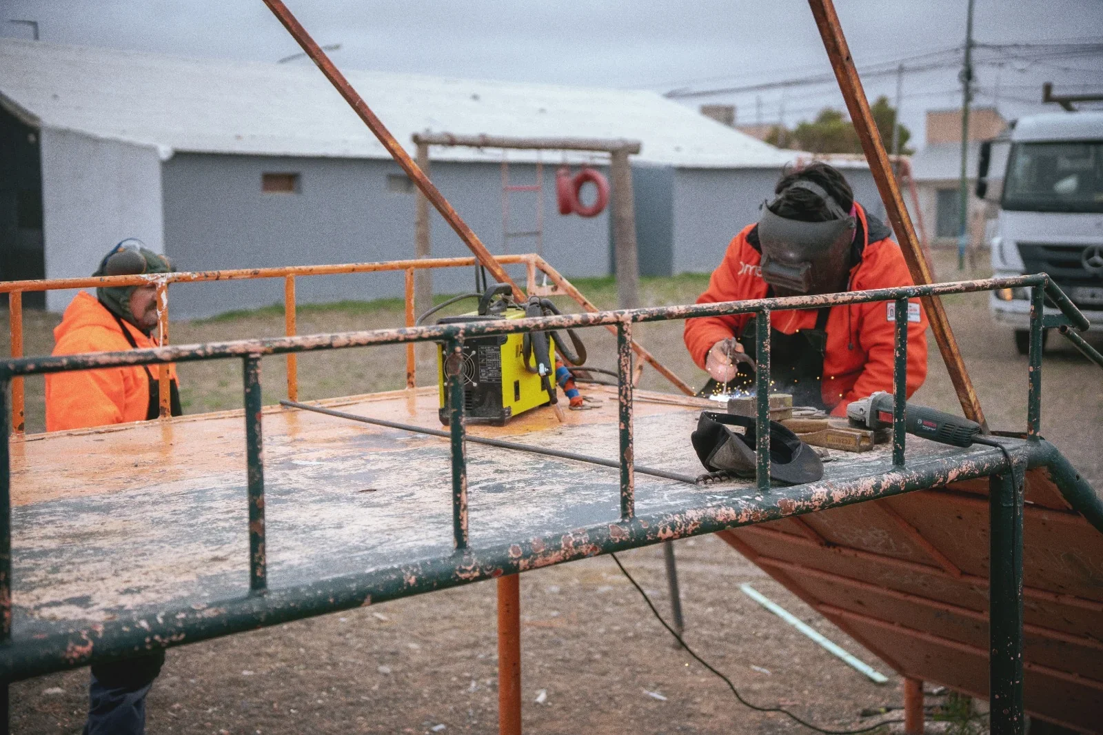Obrero con casco de soldador repara una estructura metálica de juegos infantiles en el barrio 3 de Abril, Rawson.
