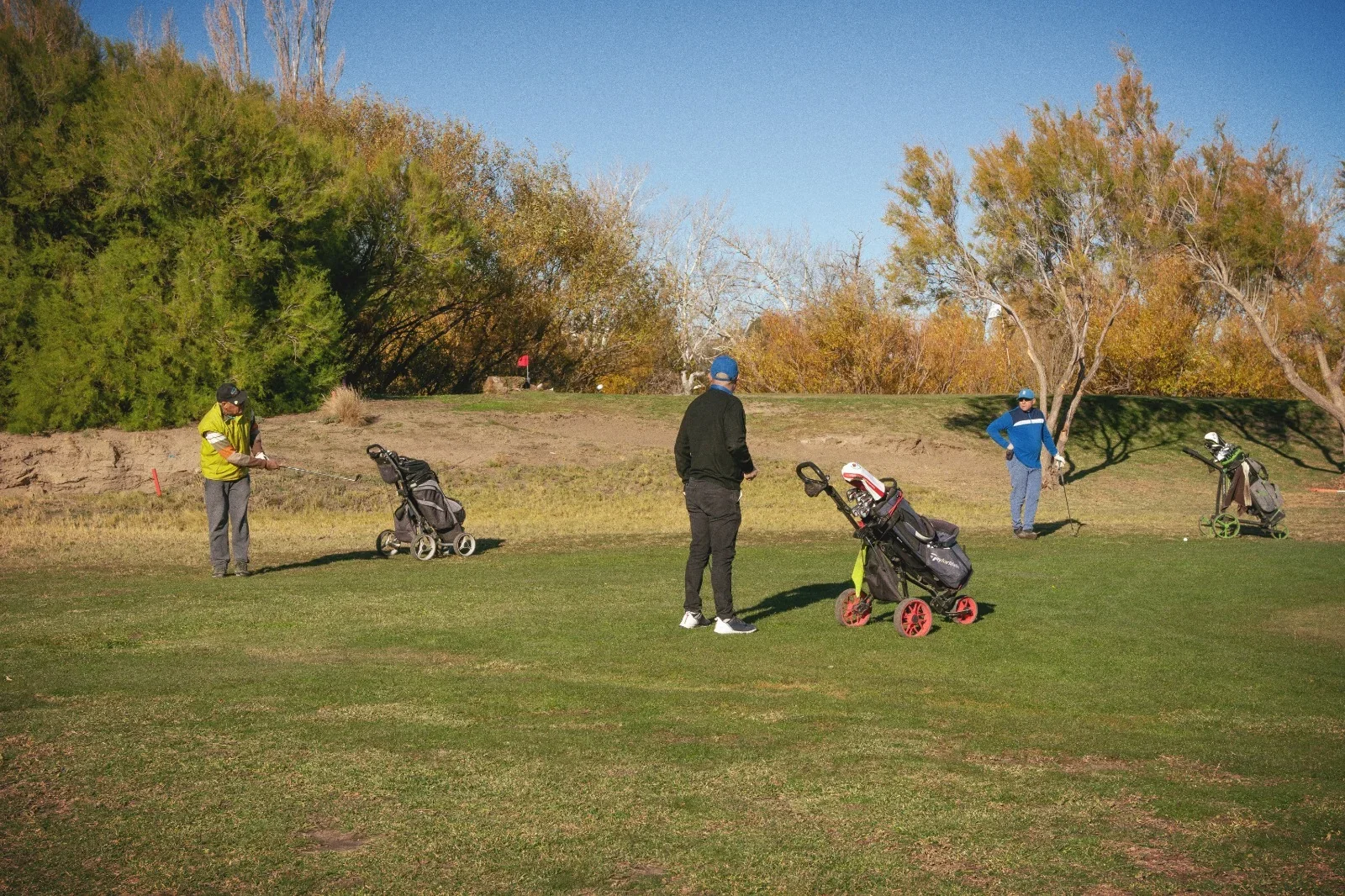 Tres golfistas con sus bolsas de palos en el campo del Tamariscos Golf Club durante el torneo por su décimo aniversario.