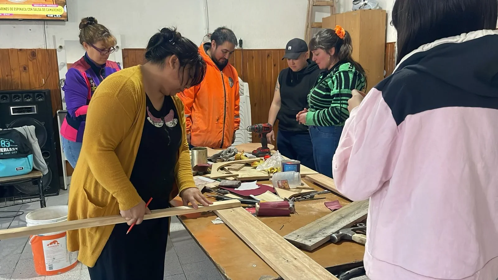 Mujeres y un instructor en un taller de Rawson manipulando maderas y herramientas del programa Yo Puedo.