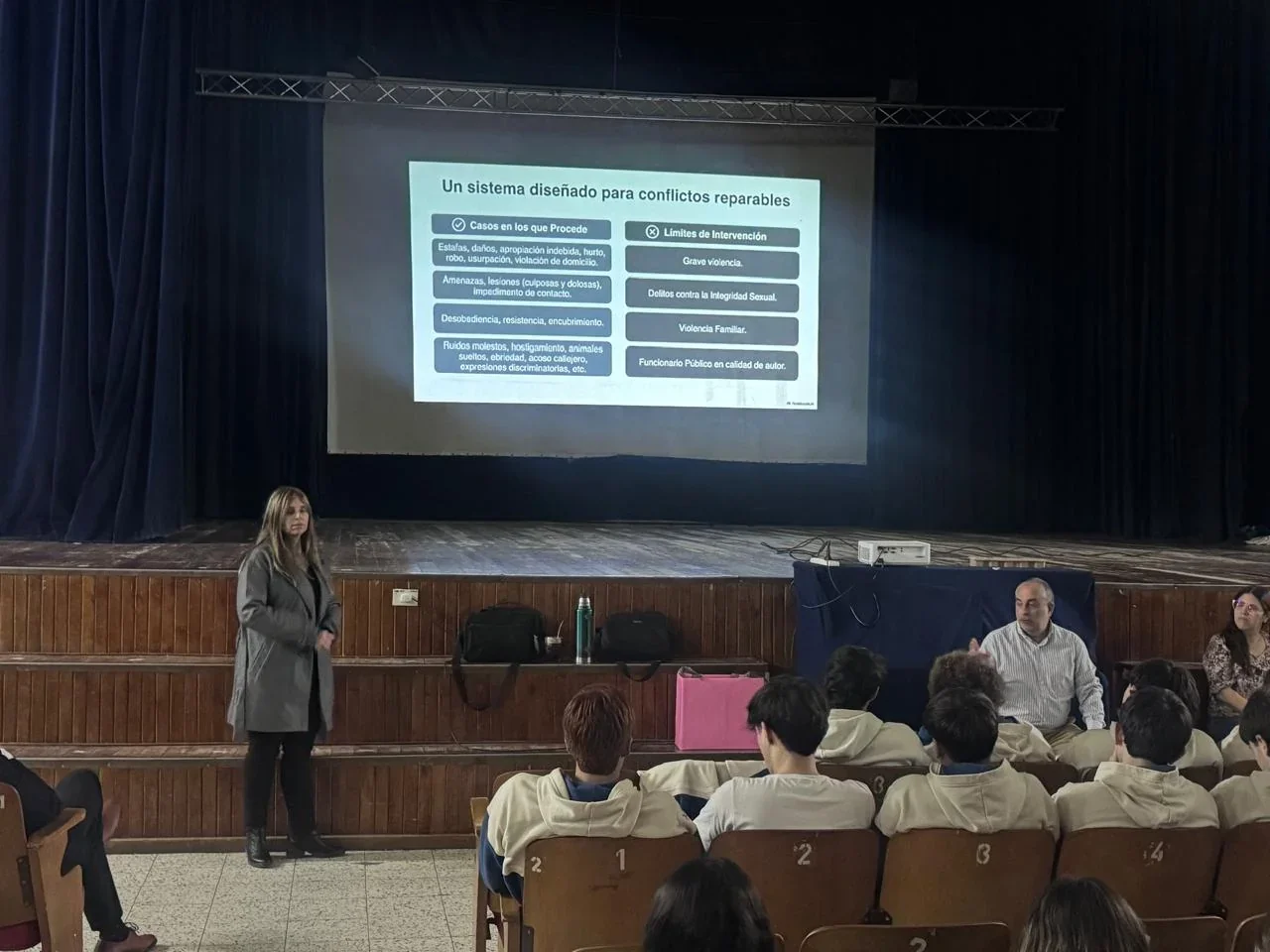 Una profesional de la Fiscalía brinda una charla a alumnos del Instituto María Auxiliadora frente a una pantalla.