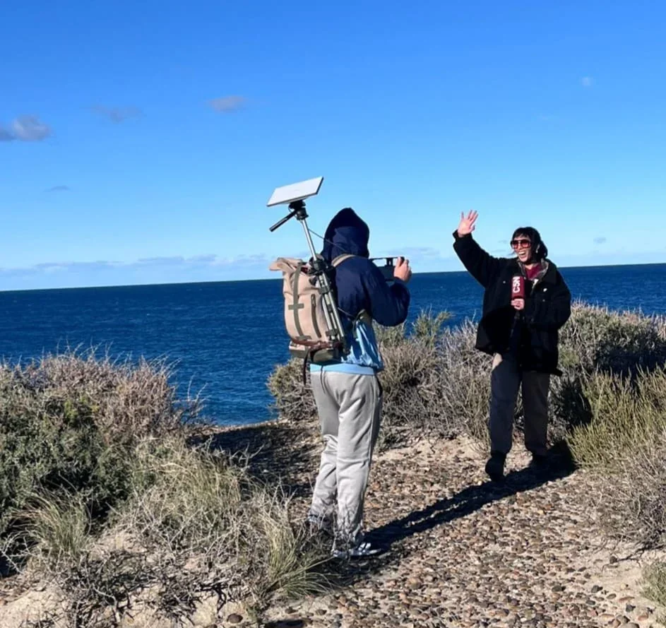 Periodista de C5N transmitiendo en vivo junto a un camarógrafo en la costa de Puerto Madryn para la temporada de ballenas.