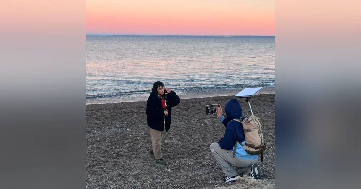 Puerto Madryn: C5N transmitió en vivo la temporada de ballenas 2026 Periodista Luciana Avilés con micrófono de C5N siendo filmada en la playa de Puerto Madryn al atardecer.