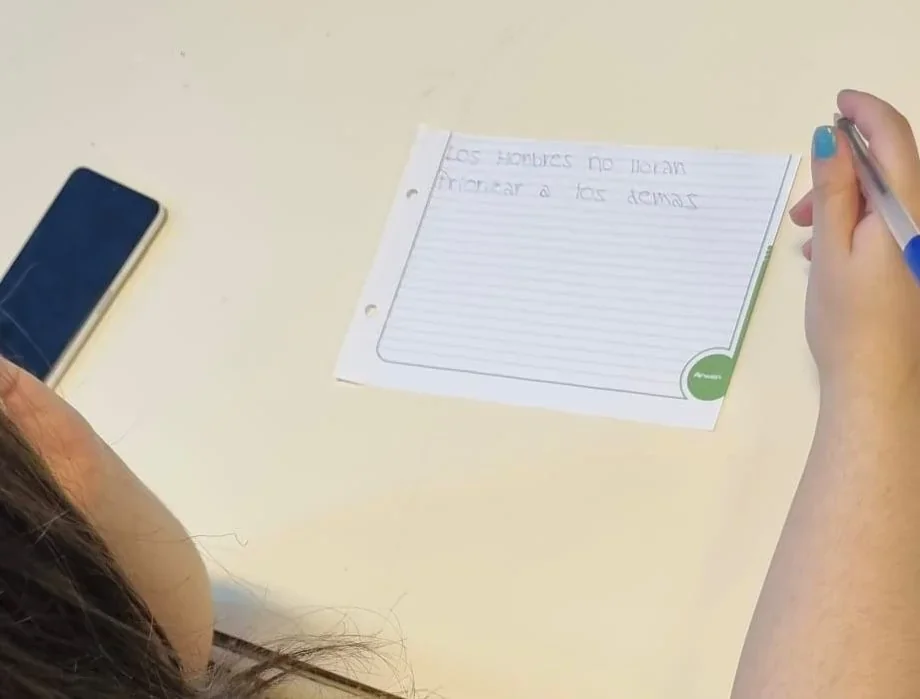 Persona escribiendo en una hoja de papel frases sobre estereotipos durante el taller Límites que Cuidan en Puerto Madryn.