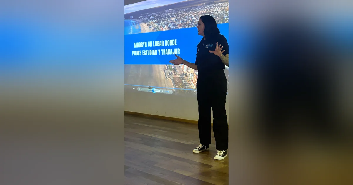 Puerto Madryn: Expo Itinerante del CGU recorre escuelas secundarias Expositora del CGU frente a una pantalla con el texto 'Madryn un lugar donde podes estudiar y trabajar'.