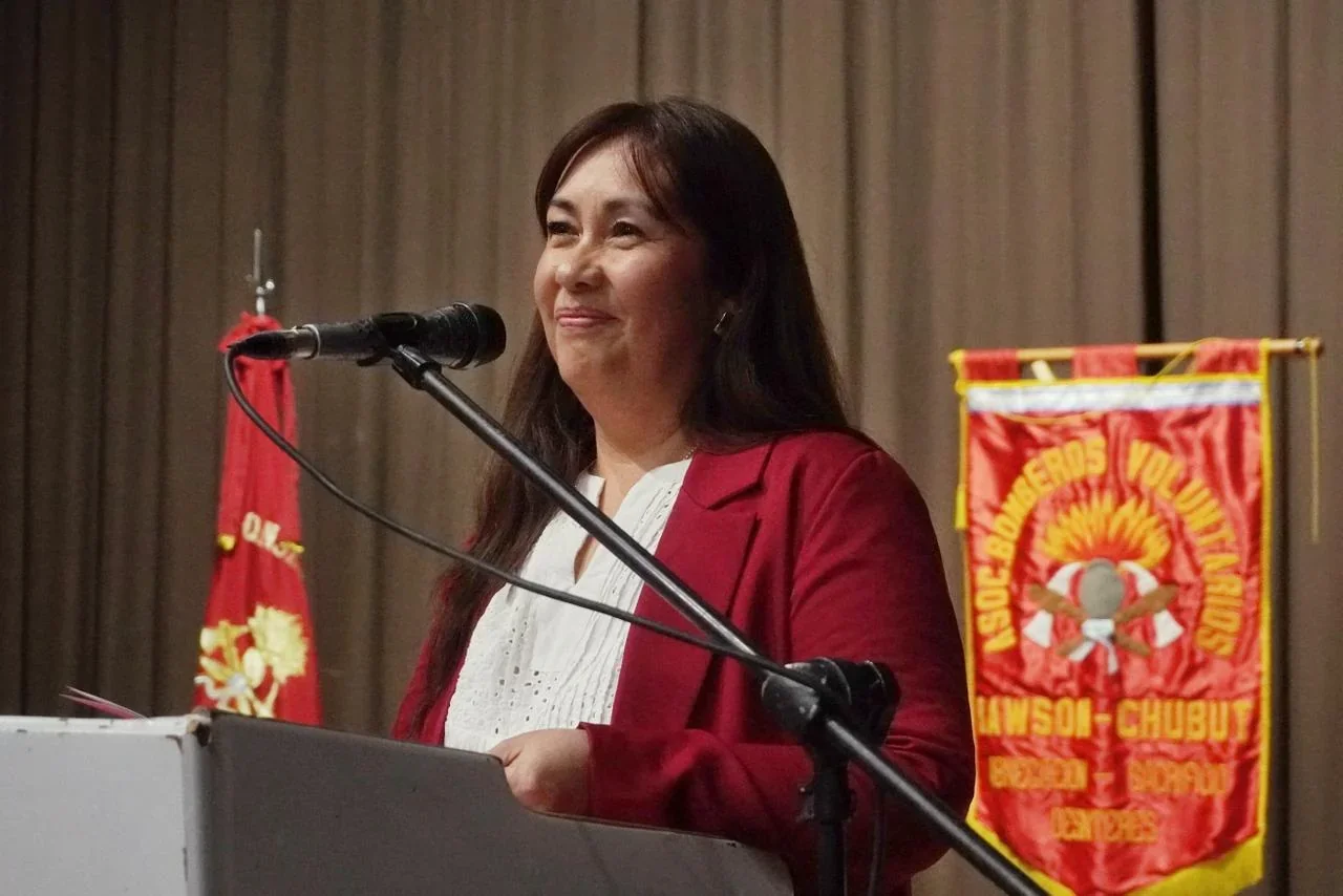 Anahí Bustos, presidenta de los Bomberos Voluntarios de Rawson, hablando frente a un micrófono en el acto de aniversario.