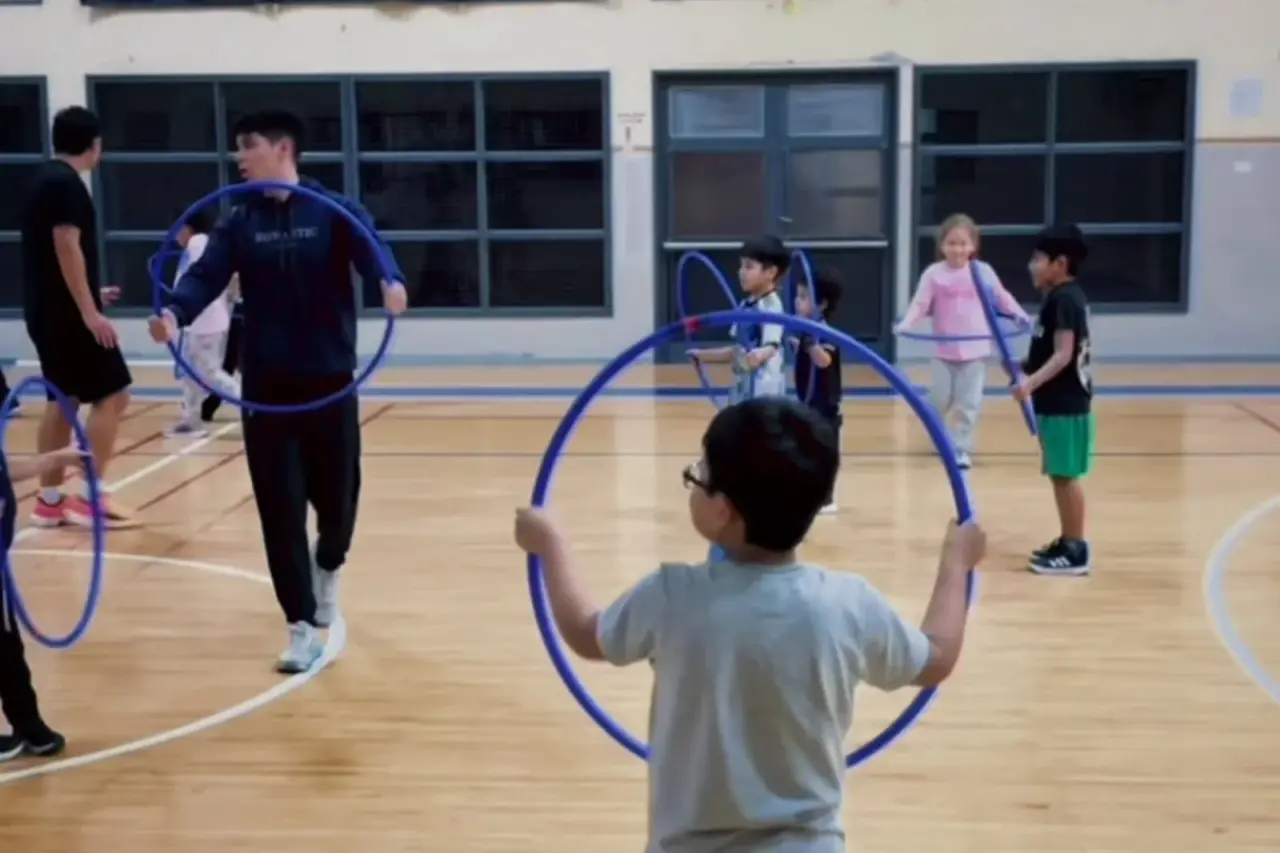 Niños y un instructor con aros azules en una cancha deportiva durante la Escuela de Iniciación Deportiva en Rawson.
