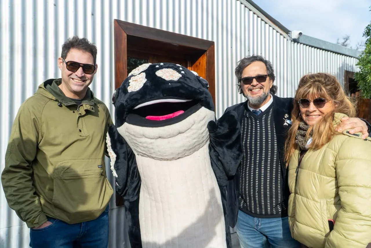 Tres personas posan junto a una mascota de ballena franca austral durante el lanzamiento de temporada en Puerto Pirámides.