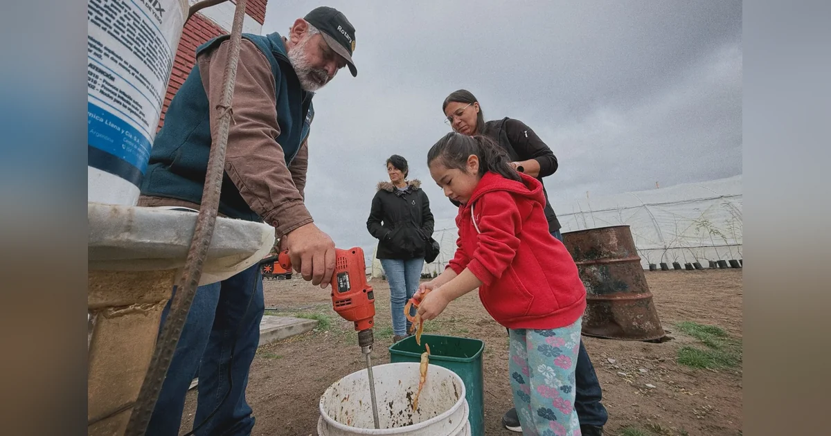 Rawson: Taller de compostaje domiciliario convocó a más de 25 vecinos Un hombre con gorra de Rotary y una niña perforan un recipiente blanco en el taller de compostaje de Rawson.