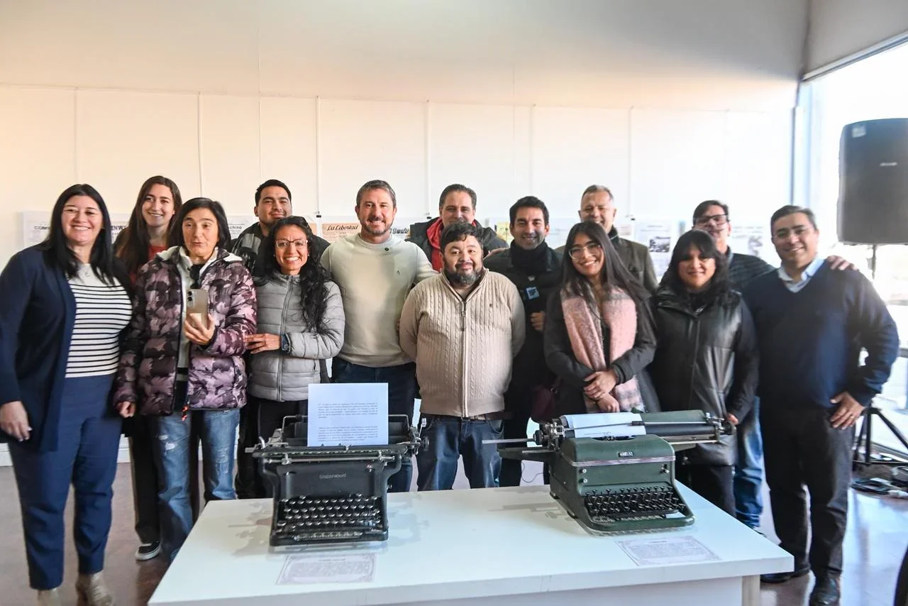 Grupo de personas posando junto a dos máquinas de escribir antiguas en la muestra Memoria impresa de una ciudad.