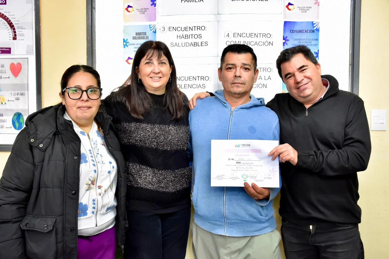 Cuatro personas posan en el CIC Menfa de Trelew; un hombre sostiene un certificado de los talleres de crianza.