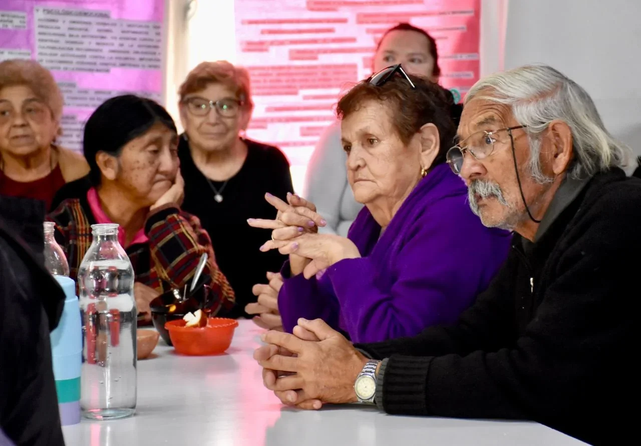 Grupo de personas mayores sentadas en una mesa durante una jornada de sensibilización sobre el buen trato en Trelew.