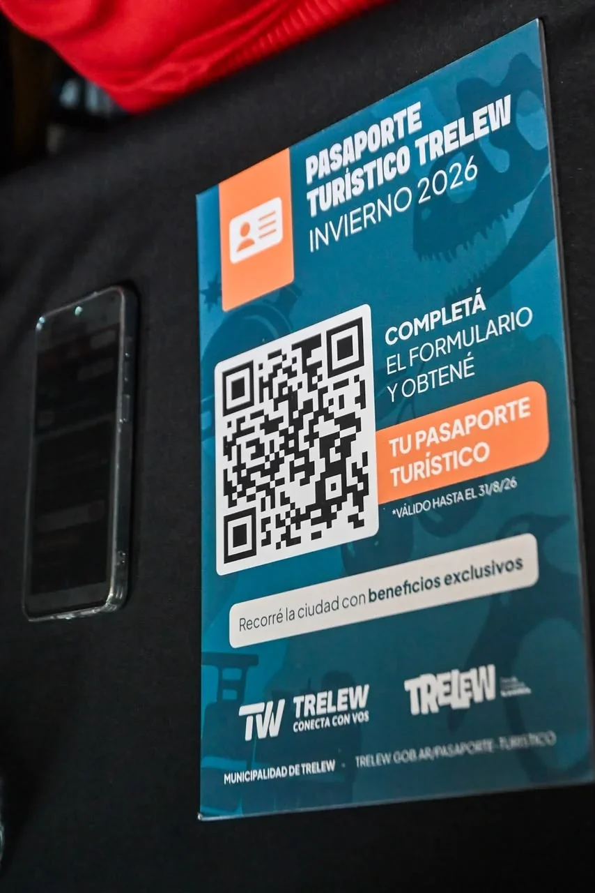 Folleto del Pasaporte Turístico Trelew Invierno 2026 con un código QR y un teléfono móvil al lado sobre fondo negro.