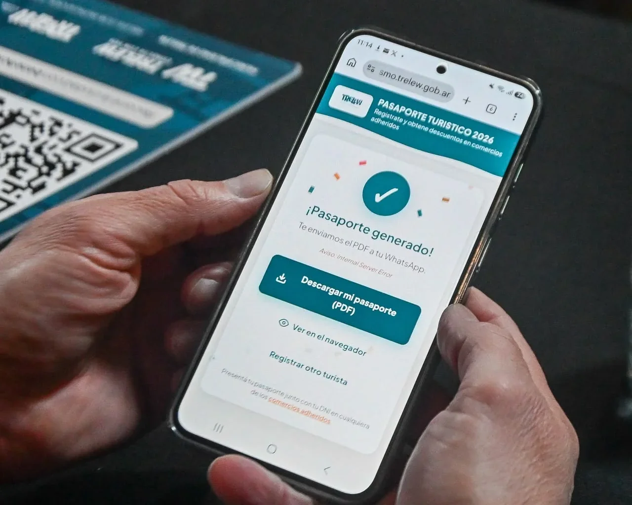 Manos sosteniendo un smartphone que muestra la confirmación de generación del Pasaporte Turístico de Trelew Invierno 2026.