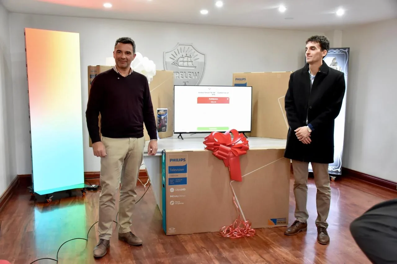 Dos hombres posan junto a una Smart TV Philips y cajas de premios en el Municipio de Trelew.