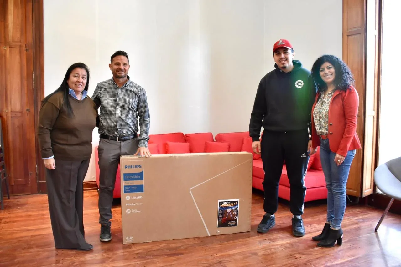 Funcionarios municipales de Trelew y un vecino junto a una caja de Smart TV Philips de 50 pulgadas entregada como premio.