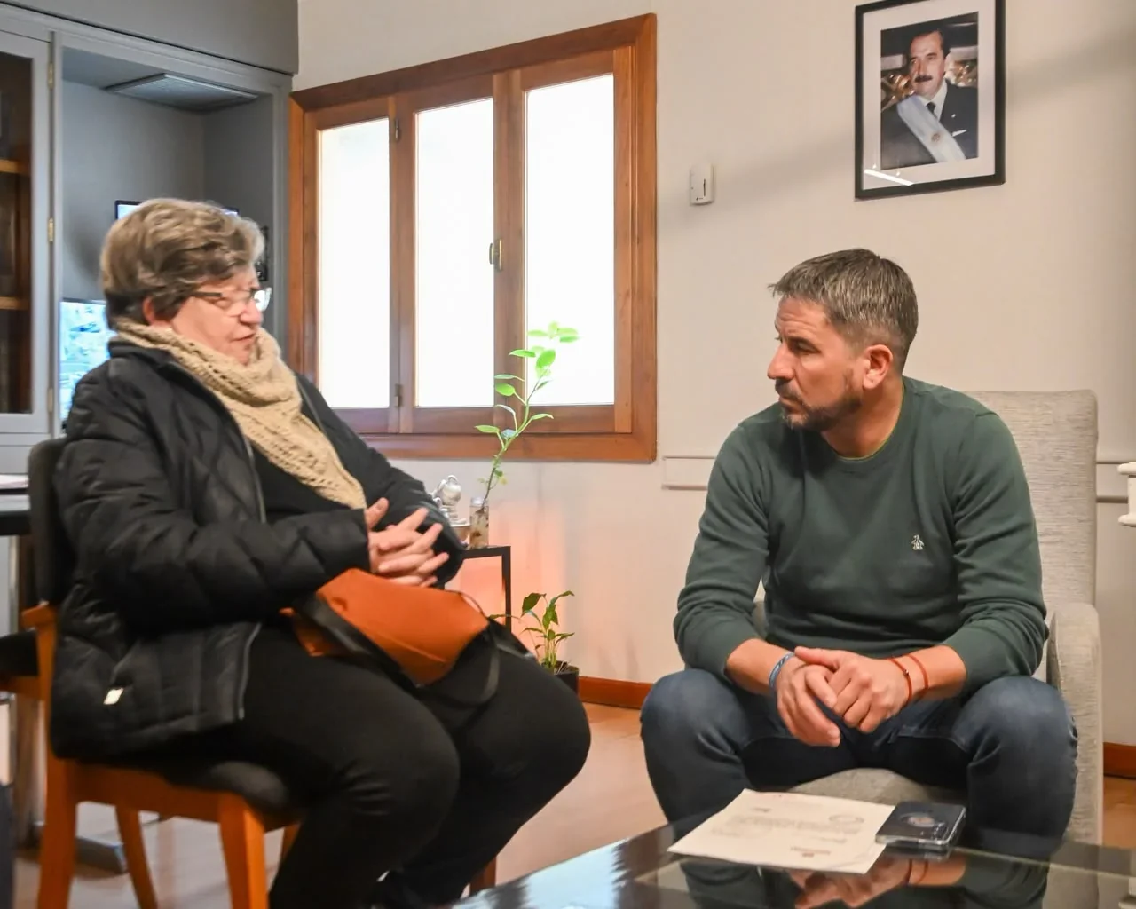 El intendente Gerardo Merino mantiene una reunión con Julia Arenas, presidenta de AJURPE Trelew, en una oficina.
