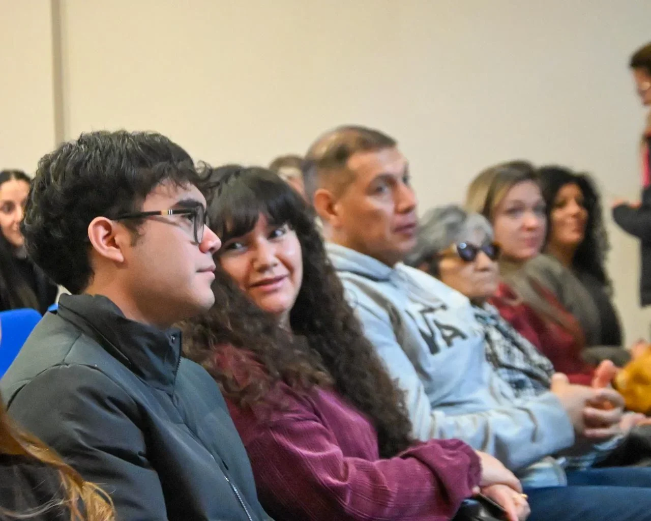 Familias de Trelew sentadas en un salón durante el acto de entrega de títulos de propiedad de viviendas.