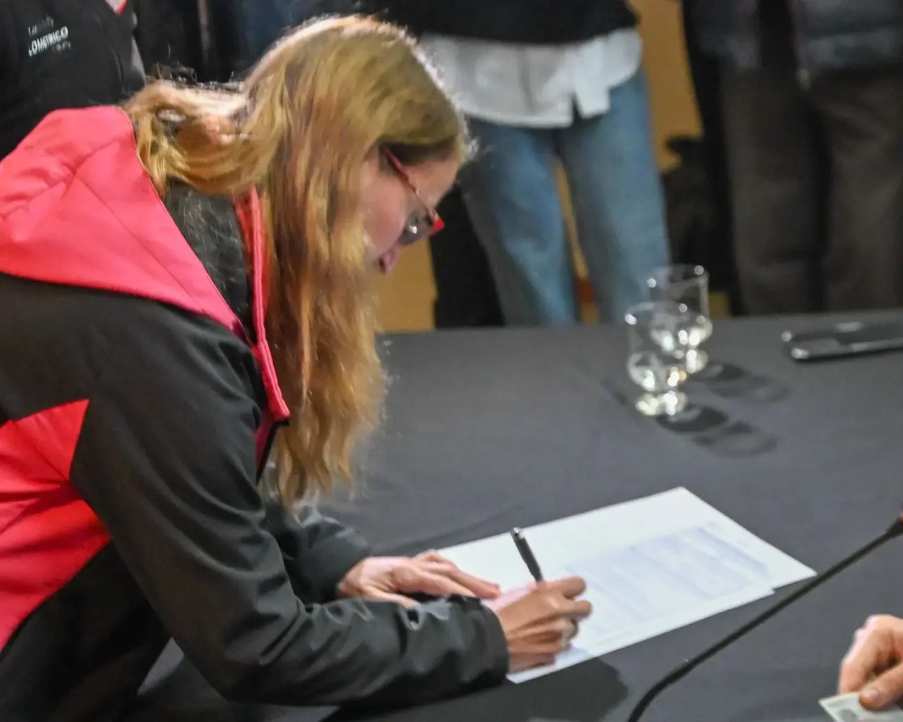 Mujer firma un documento de propiedad sobre una mesa durante el acto de regularización habitacional en Trelew.