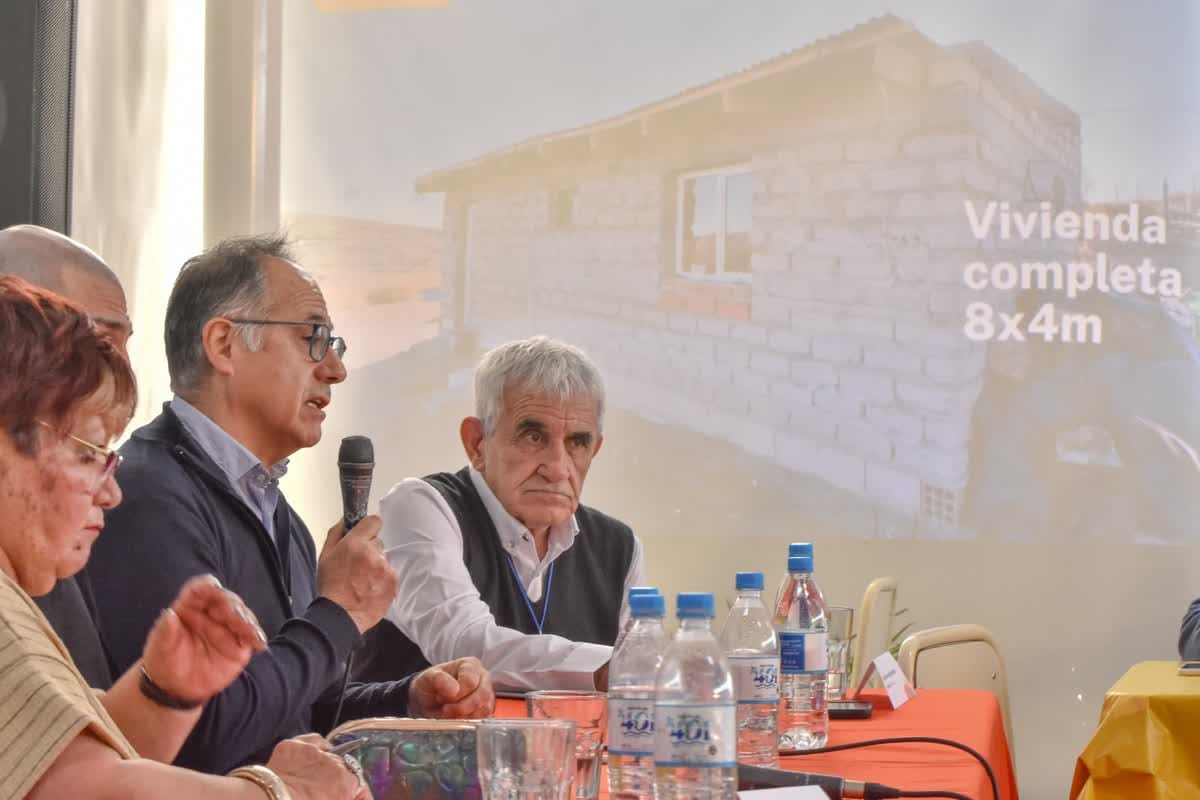 Hombre con anteojos hablando por micrófono junto a otros integrantes