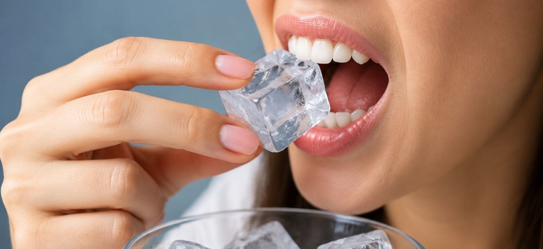 Persona llevándose un cubo de hielo a la boca